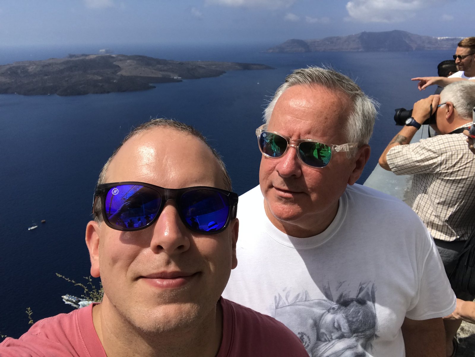 DJ Falister giving JD McArrell a skeptical, 'what are you talking about' look on a cliffside in Santorini, ocean and caldera behind them.